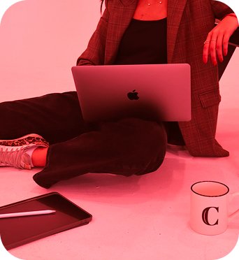 Cecile sitting on the floor working on a laptop, with a tablet and a mug nearby